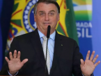 Bolsonaro sorrindo com as mãos para cima em um palanque, ele está de terno preto