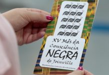 Mês da Consciência Negra de Joinville inicia nesta sexta-feira; confira programação Mulher segura panfleto sobre o XV mês da consciência negra de Joinville