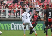 Atleta do JEC faz passe com a bola. Camisa 5 do Figueirense e camisa 19 do Joinville observam a bola.