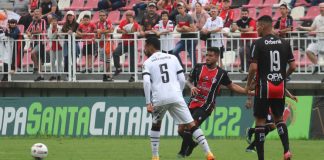 Atleta do JEC faz passe com a bola. Camisa 5 do Figueirense e camisa 19 do Joinville observam a bola.