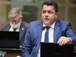 Ivan Naatz falando ao microfone em um púpito, ele está usando palitó e gravata azul