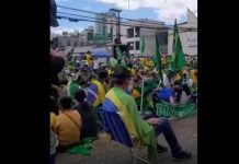 manifestantes sentados na rua, com cadeiras de pria e no asfalto, com bandeiras do brasil