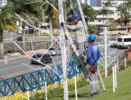 Dois homens um subindo uma escada que está encostada em um poste e o outro está no chão olhando para cima. Eles estão instalando luzes para o natal em Joinville