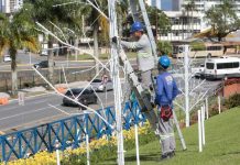 Decoração de Natal em Joinville terá recorde com mais de 1 milhão de luzes Dois homens um subindo uma escada que está encostada em um poste e o outro está no chão olhando para cima. Eles estão instalando luzes para o natal em Joinville