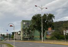 Rua de Joinville com céu com nuvens para ilustrar o tempo em Joinville. Prédio verde antigo atrás de uma árvore.