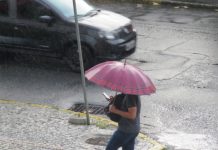 previsão do tempo em joinville. Pessoa andando com um guarda-chuva, mexendo no celular na rua.