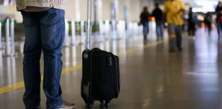 homem em pé com mala de rodinhas no aeroporto