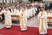 três padres olhando para o altar e o povo sentado nas cadeiras da igreja