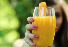 mulher segurando copo de suco de laranja com a mão direita