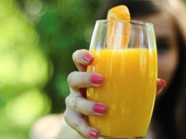 mulher segurando copo de suco de laranja com a mão direita