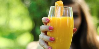 mulher segurando copo de suco de laranja com a mão direita