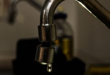 Gota sai em torneira, com detergente ao fundo