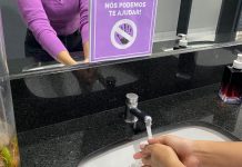 mulher lavando as mãos de frente para um cartaz que diz "nós podemos de ajudar" em casos de assédio