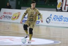 O atleta Pato domina a bola no meio da quadra de futsal, ele utiliza um uniforme dourado do JEC Futsal.