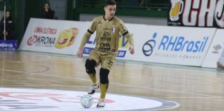 O atleta Pato domina a bola no meio da quadra de futsal, ele utiliza um uniforme dourado do JEC Futsal.