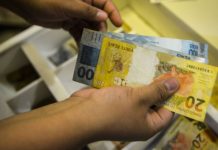 Pessoa segura com as mãos duas notas de R$ 100 e uma nota de R$ 20